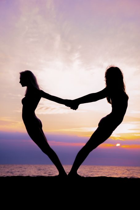 Dos siluetas femeninas de espaldas, unidas de las manos, formando un corazón al atardecer.