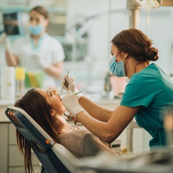 Dentista atiende a una paciente en una clínica dental, con otra persona al fondo.