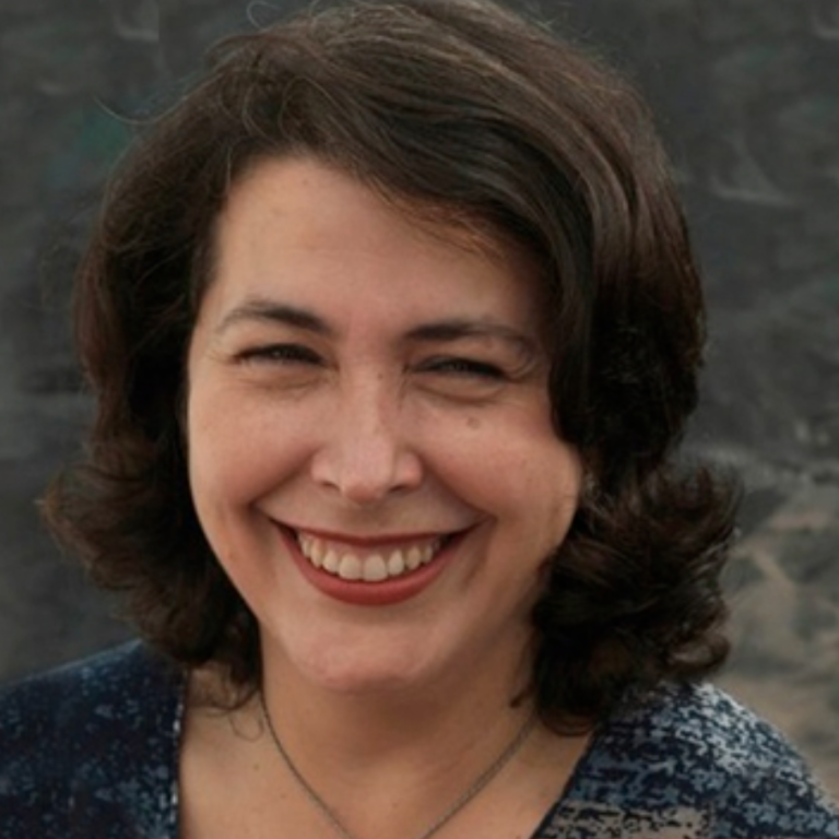 Mujer sonriente con cabello oscuro y rizado, vestida con una blusa azul.