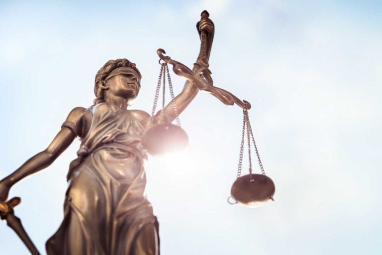 Estatua de la Justicia sosteniendo balanzas bajo un cielo claro.